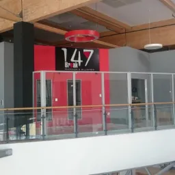 Wnętrze biurowe z logo '147 Break Snooker & Billiards' na czerwonej ścianie, widok z góry przez szklaną balustradę, drewniane belki stropowe i okrągłe lampy sufitowe.