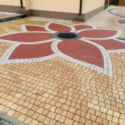 Wzór kwiatu ułożony z czerwonej i szarej kostki brukowej na podjeździe z żółtej kostki brukowej.