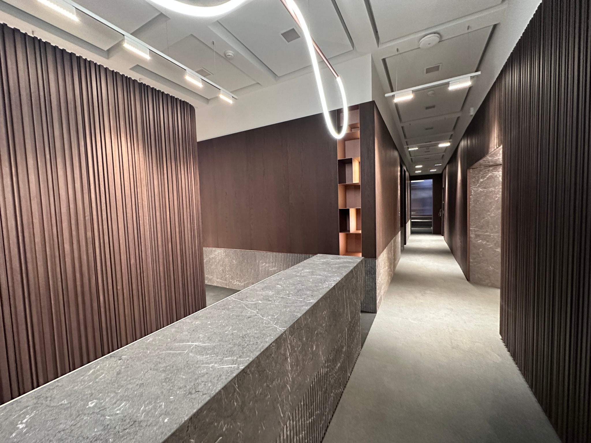 Nowoczesne wnętrze biurowe z panelami ściennymi w odcieniach brązu, marmurowym blatem i designerskim oświetleniem LED.