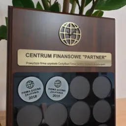 Certyfikat 'Firma Godna Zaufania' dla Centrum Finansowego 'Partner', edycje 2018 i 2019, umieszczony na drewnianej tablicy z zegarem w kształcie globu, z rośliną w tle.