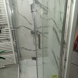 RO-STA Firma Ogólnobudowlana Starosta Roman - Kabina prysznicowa z marmurowymi płytkami na ścianach, chromowaną armaturą i grzejnikiem drabinkowym obok, zabezpieczona folią w brodziku.