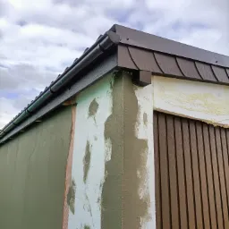 Narożnik budynku w trakcie ocieplania: widoczne fragmenty styropianu, siatki, kleju i wstępnie nałożonego tynku mineralnego w kolorze oliwkowym, brązowe panele elewacyjne imitujące drewno...