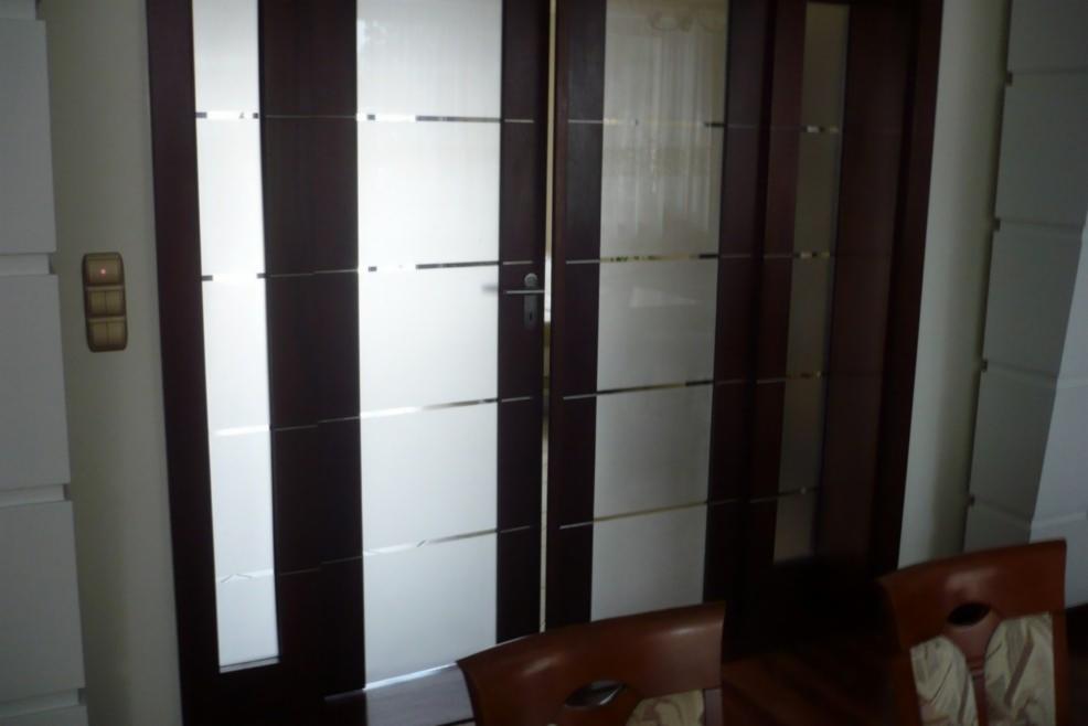 Nowoczesne, dwuskrzydłowe drzwi drewniane z poziomymi, matowymi przeszkleniami, widoczne wewnątrz pomieszczenia.