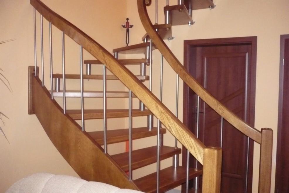 Kręte schody drewniane z metalowymi poręczami, widoczne drzwi w tle, element dekoracyjny na ścianie.