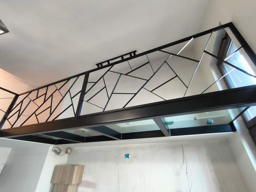 Antresola z czarną, geometryczną balustradą i szklaną podłogą, widziana z dołu. W tle surowa ściana i okno. Nietypowy wzór balustrady.