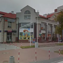 Widok na budynek z biurami i lokalami handlowymi, w tym biuro nieruchomości Krzewscy, z ulicy w pochmurny dzień.