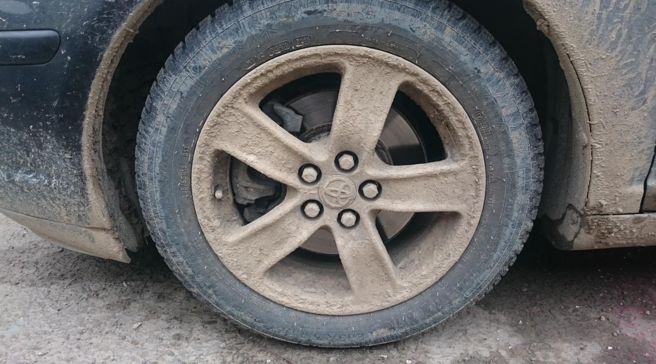 Bardzo brudne koło i fragment nadwozia samochodu Toyota, pokryte zaschniętym błotem.
