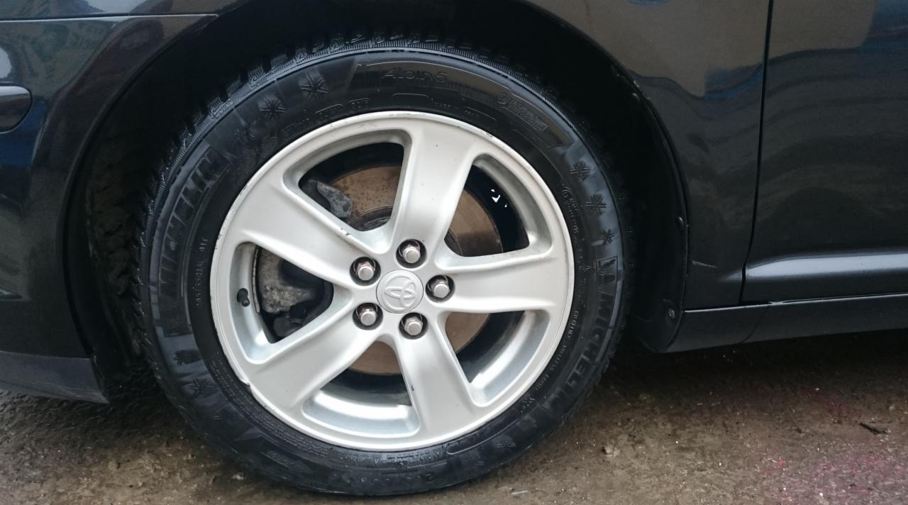 Błyszczące, mokre koło samochodu marki Toyota z aluminiową felgą o pięciu ramionach i oponą zimową z widocznym bieżnikiem.