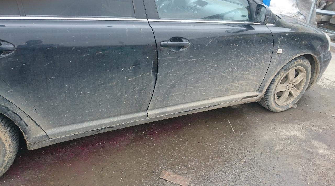 Bardzo brudny, czarny samochód osobowy z wyraźnymi śladami błota i brudu na karoserii oraz oponach, stojący na mokrej nawierzchni z widocznymi plamami.