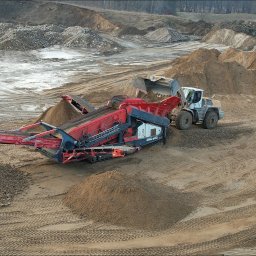 Firma Zdanpol - Przesiewacz wibracyjny oddziela materiał sypki na frakcje, ładowarka podaje urobek, w tle teren budowy z hałdami urobku.