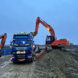 KZ Zdanpol Sp. z o.o. - Pomarańczowa koparka Doosan DX225LC nabiera ziemię na wywrotkę Zdanpol Scania R620 w Kolbudach, w tle widoczny teren budowy.
