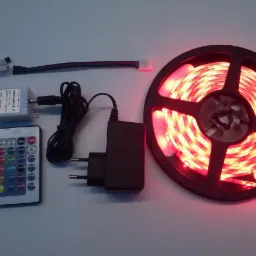 Zestaw oświetleniowy LED RGB na szpuli z pilotem, zasilaczem i kontrolerem, prezentacja produktu na jasnym tle.