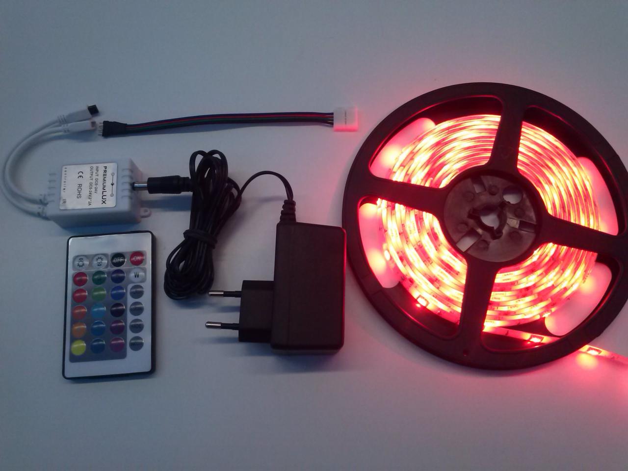 Zestaw oświetleniowy LED RGB na szpuli z pilotem, zasilaczem i kontrolerem, prezentacja produktu na jasnym tle.