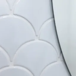 Białe, błyszczące płytki w kształcie rybiej łuski na ścianie w Kielcach, częściowo zasłonięte przez krawędź białego elementu wyposażenia.