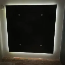 Czarny sufit podwieszany z oświetleniem LED obwodowym i czterema punktowymi lampami, widoczny fragment ściany z cegły i grzejnika.