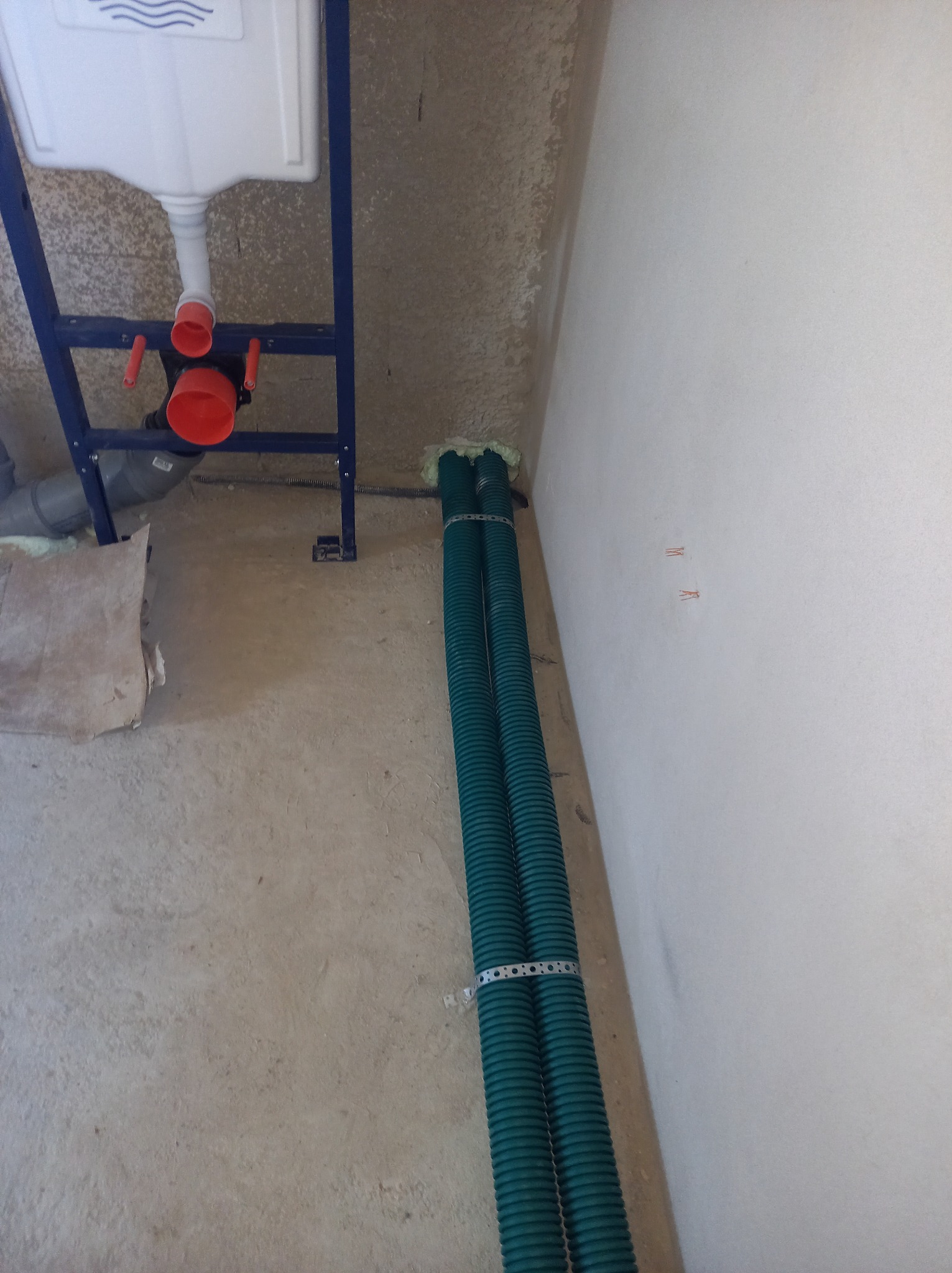 Stelaż podtynkowy WC z widocznymi rurami wentylacyjnymi, zabezpieczonymi pianką montażową przy przejściu przez ścianę, w surowym stanie wykończenia.