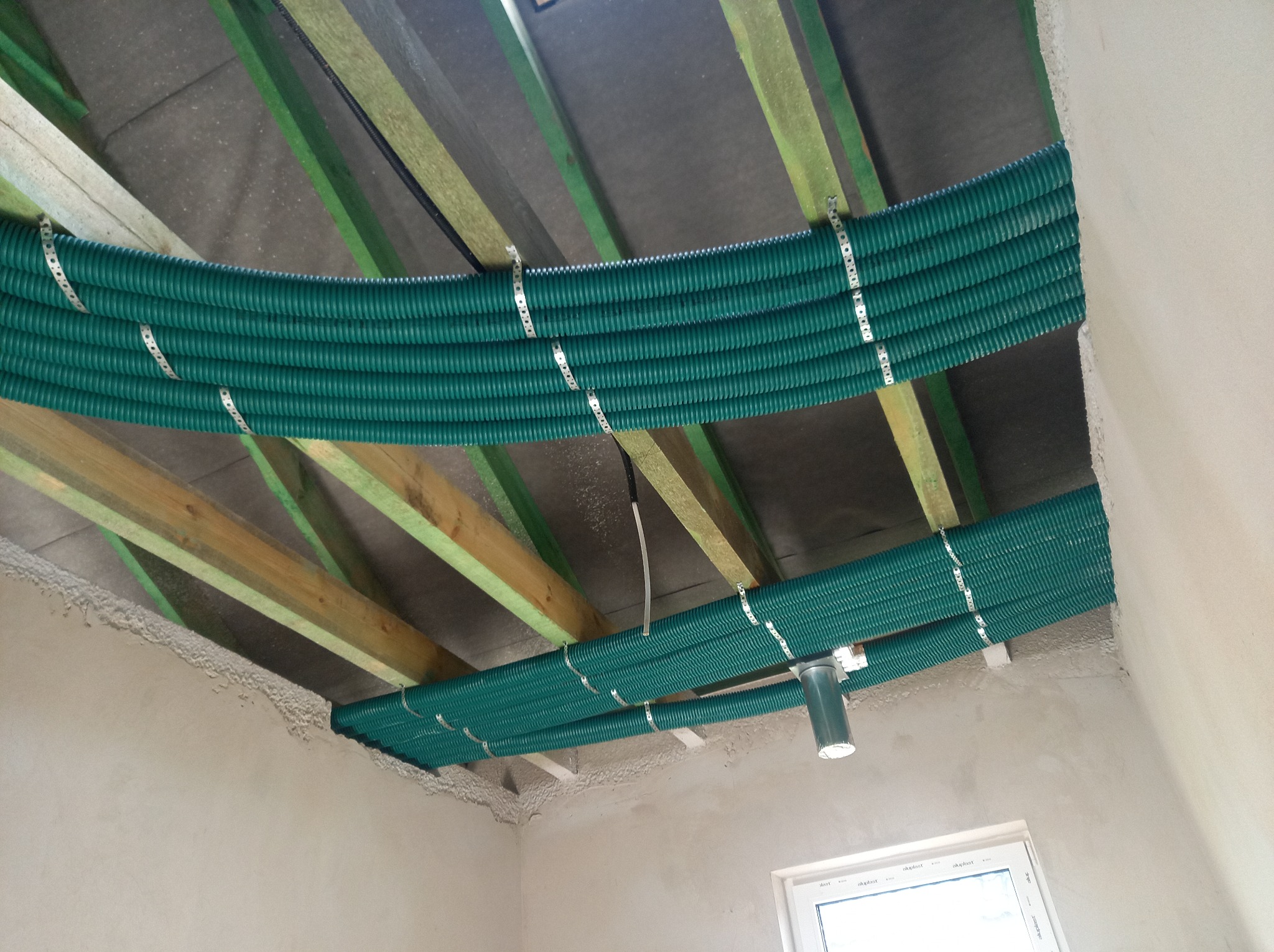 Zielone rury wentylacyjne przymocowane metalowymi opaskami do drewnianej konstrukcji pod stropem w surowym wnętrzu.