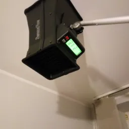 Czarny anemostat pomiarowy marki SwemaFlow zamocowany do sufitu na metalowym ramieniu, wyświetlający zielony odczyt 21.2.