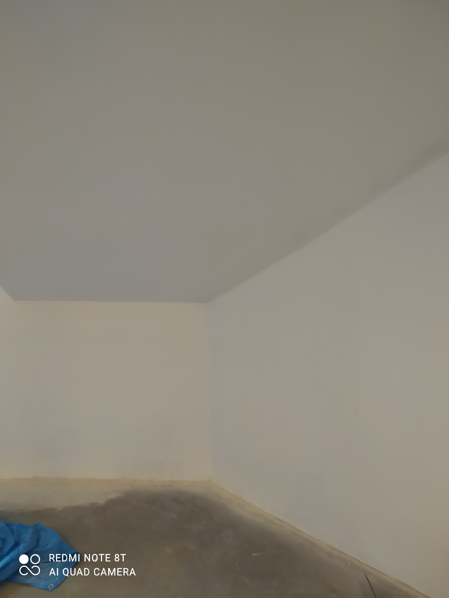 Wnętrze pokoju po nałożeniu gładzi gipsowych na ścianach i suficie, z widoczną niebieską folią ochronną na podłodze w rogu.