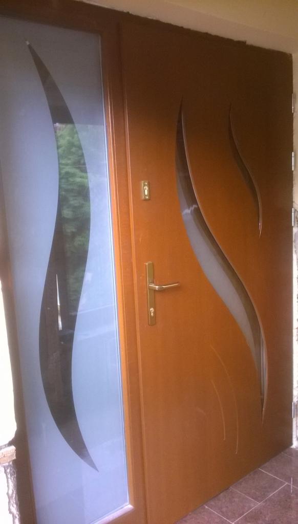 Brązowe drzwi wejściowe z przeszkleniem o falistym wzorze, widoczne złote okucia i zamek.