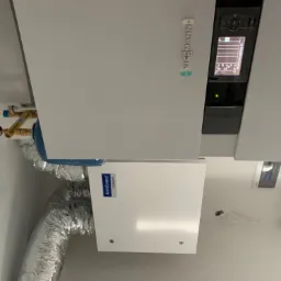 Zamontowana jednostka rekuperacyjna Komfovent Domext z podłączonymi przewodami wentylacyjnymi, obok panel sterowania Viessmann z widocznym wyświetlaczem.