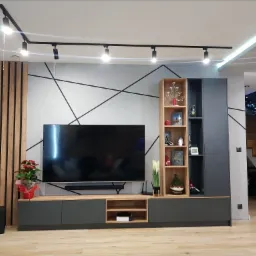 Szara zabudowa meblowa pod telewizor z drewnianymi akcentami, oświetleniem punktowym i dekoracyjną ścianą z geometrycznym wzorem w nowoczesnym salonie.