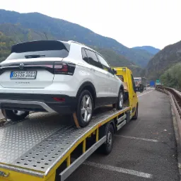 Biały Volkswagen T-Cross zabezpieczony pasami na żółtej lawecie, w tle górzysty krajobraz.