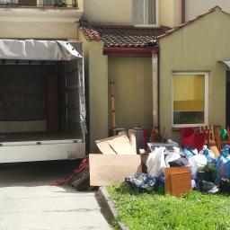 Carolus Magnus Sp. z o.o - Otwarta paka busa na tle budynku z zebranymi rzeczami do transportu: worki, meble, kartony, dywan.