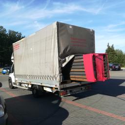 Carolus Magnus Sp. z o.o - Ciężarówka z plandeką, z otwartą tylną klapą, załadowana elementami metalowymi w czerwonym opakowaniu, zaparkowana na parkingu w słoneczny dzień.