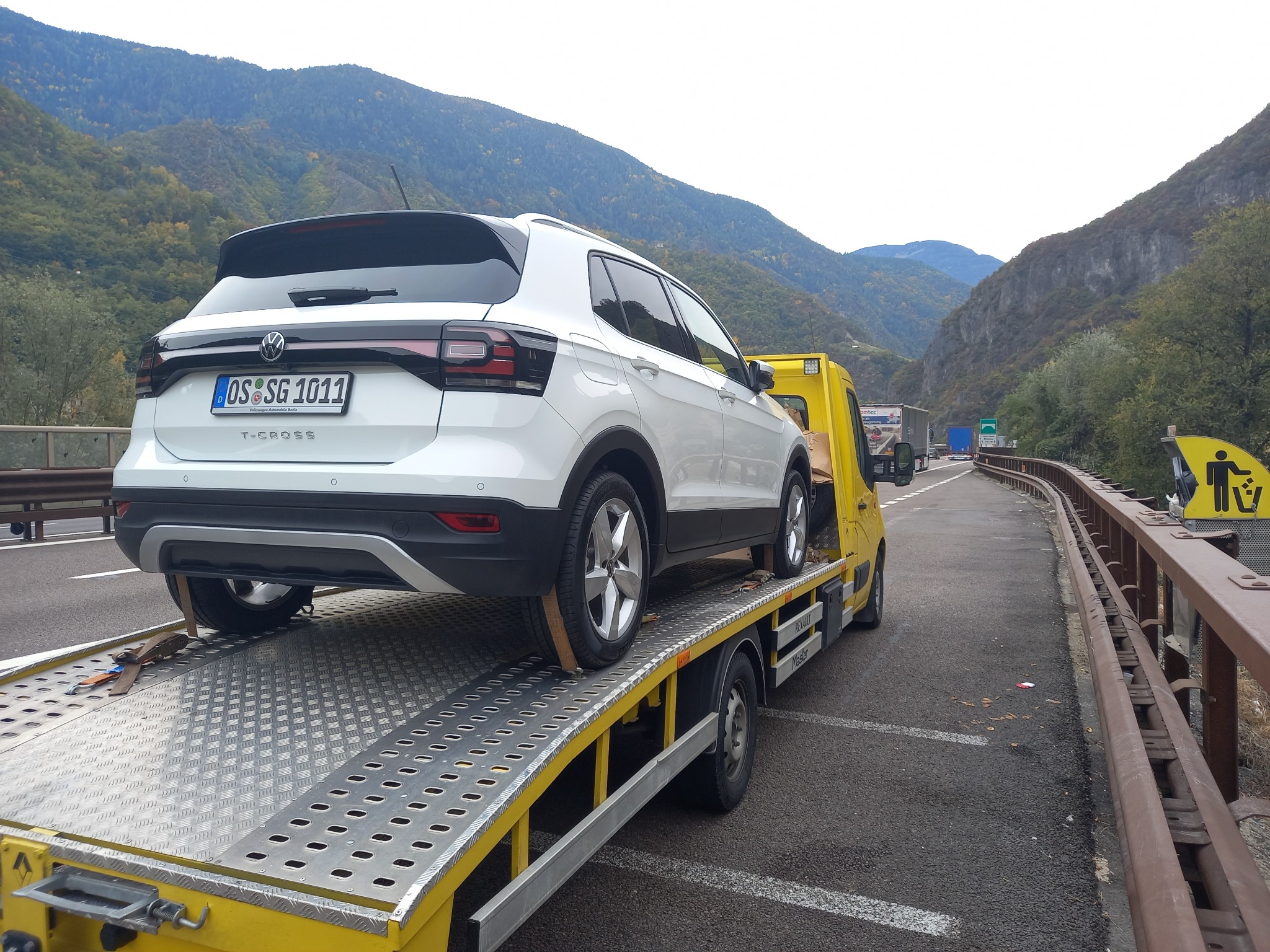 Biały Volkswagen T-Cross zabezpieczony pasami na żółtej lawecie, w tle górzysty krajobraz.