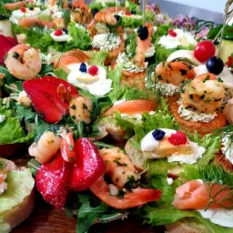 Bogato zdobione kanapeczki koktajlowe z krewetkami, łososiem, truskawkami, jajkiem i ziołami, ułożone na zielonej sałacie, widoczne z bliska.