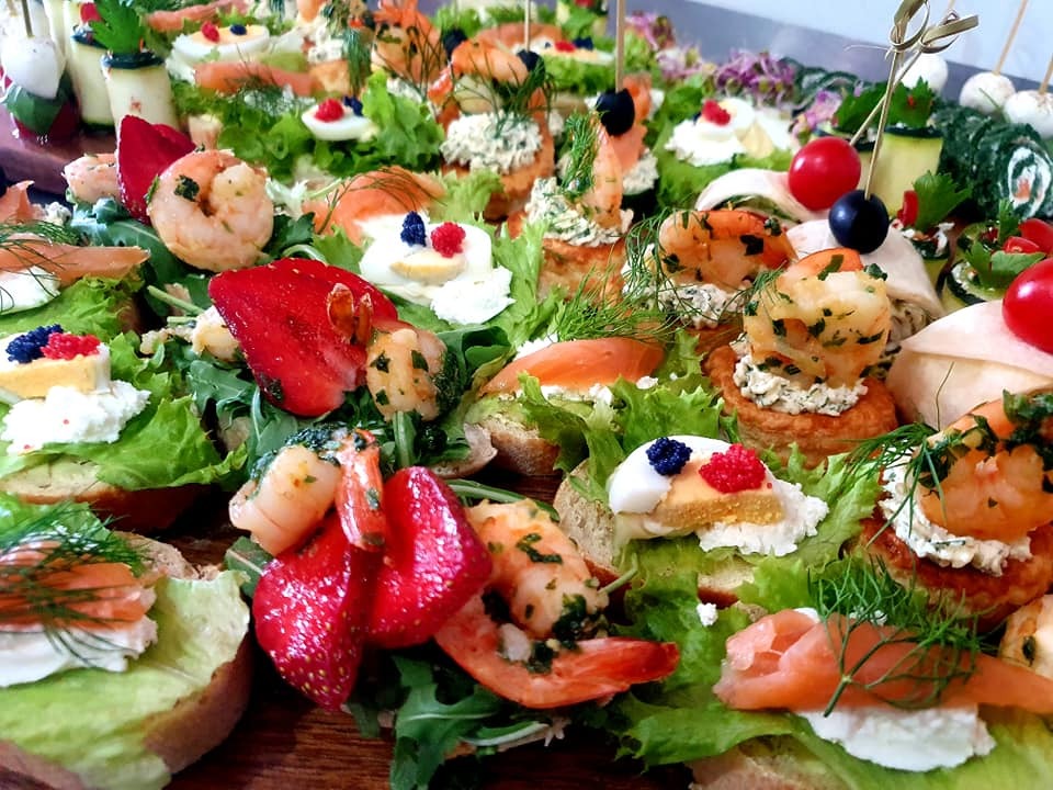 Bogato zdobione kanapeczki koktajlowe z krewetkami, łososiem, truskawkami, jajkiem i ziołami, ułożone na zielonej sałacie, widoczne z bliska.