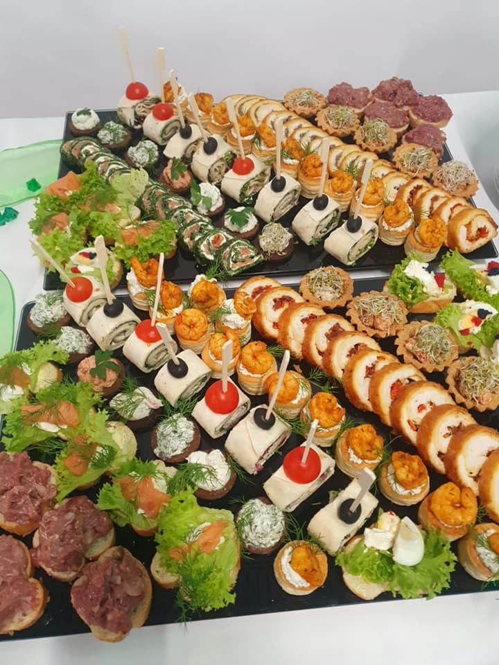 Dwa czarne prostokątne półmiski z różnorodnymi, apetycznie wyglądającymi przekąskami: roladki z łososiem i szpinakiem, mini tartaletki z pastami, kanapeczki z sałatą i krewetkami, koreczki...