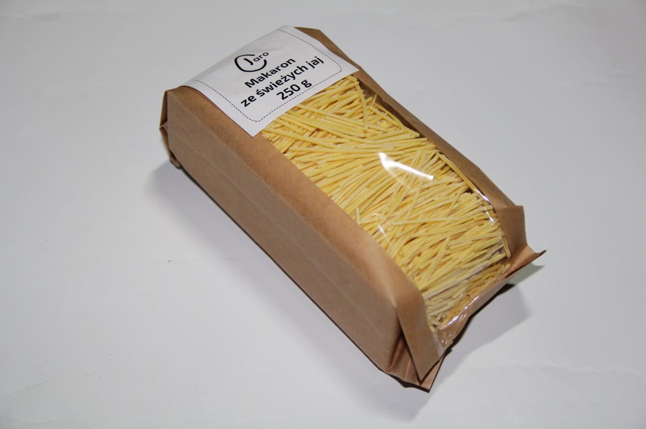 Opakowanie makaronu ze świeżych jaj o gramaturze 250g, w brązowym papierowym opakowaniu z okienkiem, widoczne nitki makaronu.