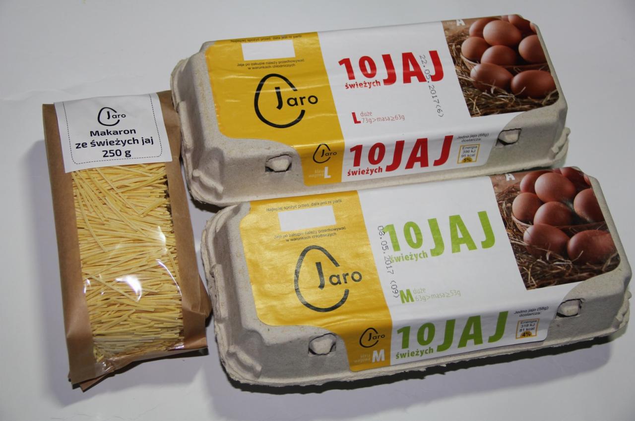 Dwa kartony świeżych jaj marki Jaro, jeden rozmiaru L, drugi M, ułożone jeden na drugim obok paczki makaronu jajecznego tej samej marki w brązowym papierowym opakowaniu z przezroczystym okienkiem.