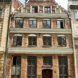 Fasada kamienicy z czerwonej cegły w stylu gotyckim z charakterystycznym szczytem schodkowym i rzędami okien.