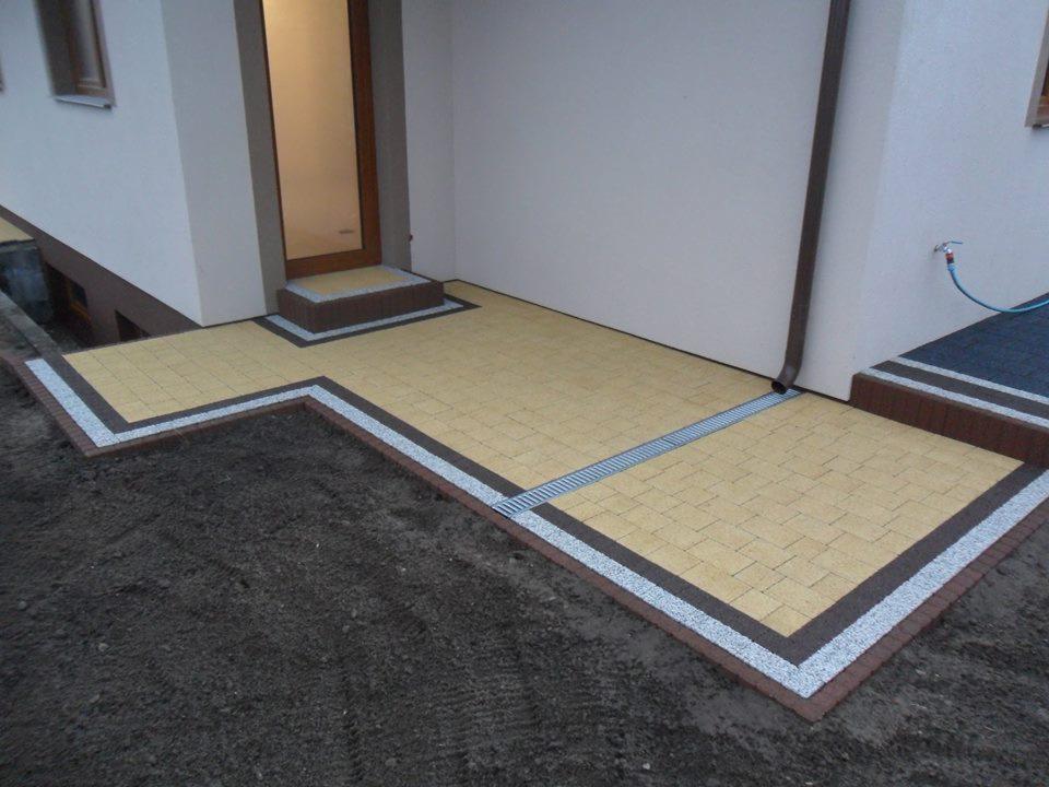 Żółta kostka brukowa ułożona na tarasie przed wejściem do domu, obrzeża z ciemniejszej kostki, widoczny odpływ liniowy