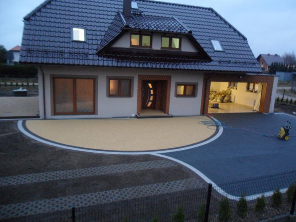 Nowoczesny dom jednorodzinny z podjazdem wyłożonym dwukolorową kostką, widoczna myjka ciśnieniowa i fragment ogrodzenia.