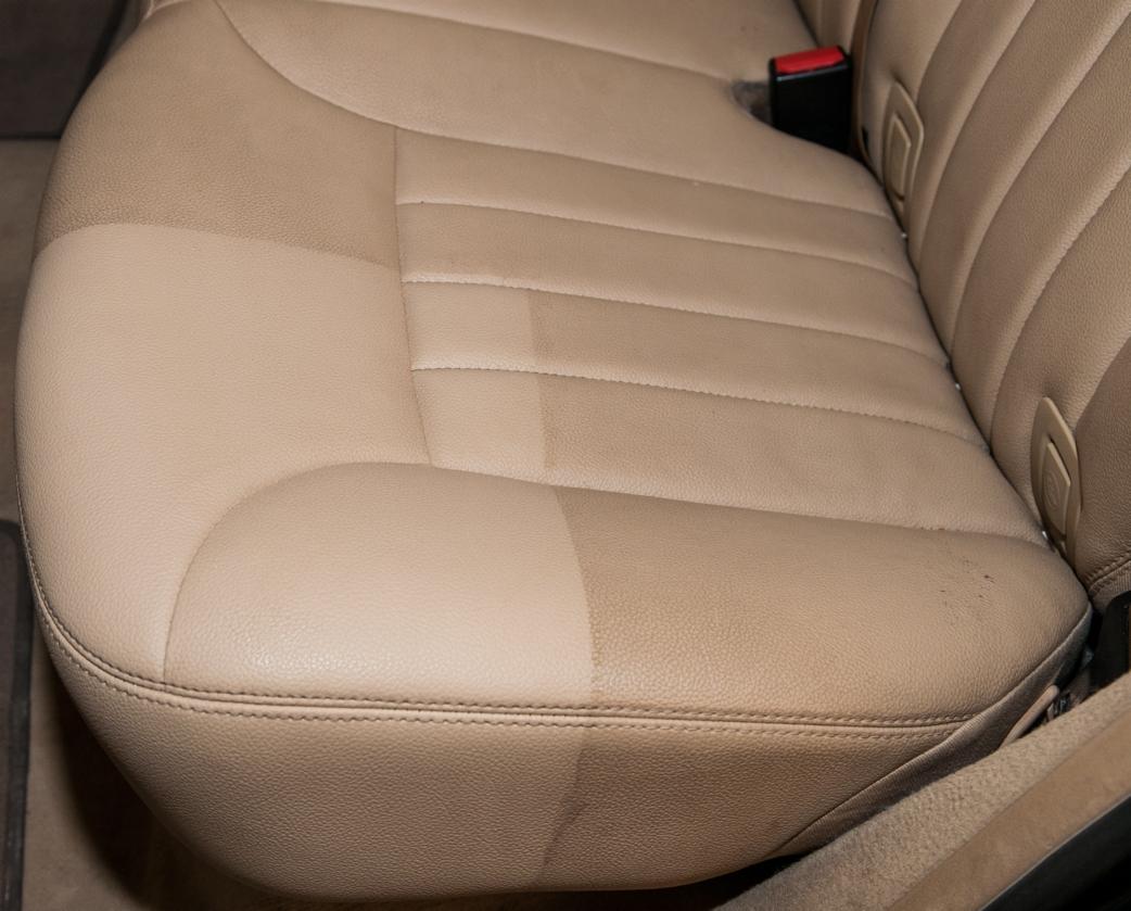 Fragment beżowego, skórzanego fotela samochodowego, ukazujący różnicę w czystości po częściowym czyszczeniu tapicerki.