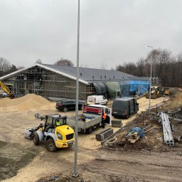 House Investments Piotr Ziółkowski - Budynek w trakcie prac elewacyjnych, widoczne rusztowania, maszyny budowlane i materiały, pochmurne niebo.