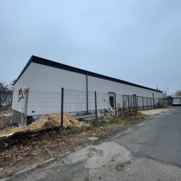 House Investments Piotr Ziółkowski - Budynek w trakcie prac elewacyjnych, widoczne rusztowania i materiały budowlane, teren częściowo ogrodzony, pochmurne niebo.