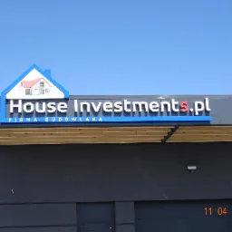 Szyld firmy budowlanej House Investments.pl z logo w kształcie domu na tle błękitnego nieba, umieszczony na szarej elewacji budynku z drewnianym podbitką.
