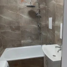 Wykończona łazienka w Gorzowie Wielkopolskim z wanną, umywalką z szafką i marmurkowymi płytkami na ścianach.