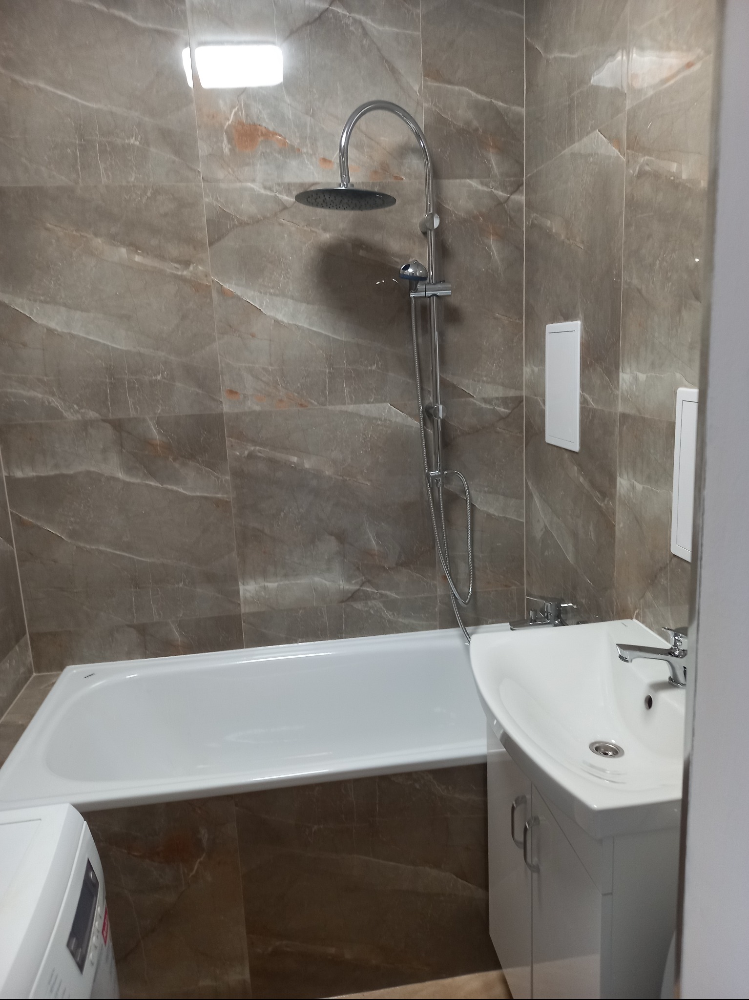 Wykończona łazienka w Gorzowie Wielkopolskim z wanną, umywalką z szafką i marmurkowymi płytkami na ścianach.