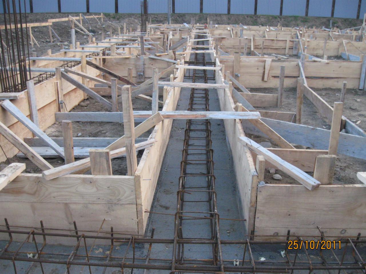 Szczegółowy widok szalunków fundamentowych zbrojonych stalą, przygotowanych do wylania betonu, w trakcie budowy domu.