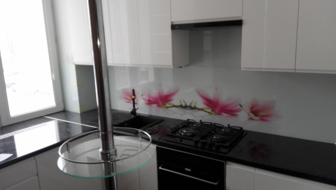 Nowoczesna biała kuchnia z czarnym blatem, szklanym panelem z motywem magnolii i chromowanym słupkiem z półkami.