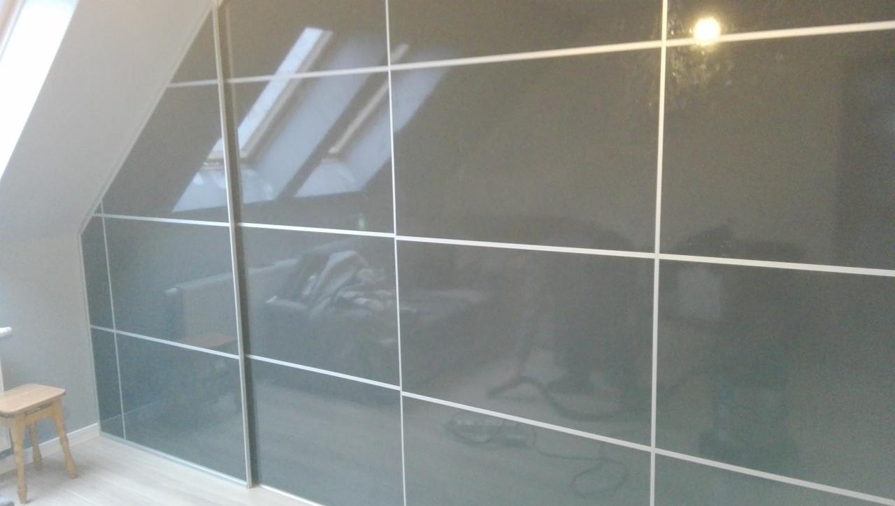 Szara szafa przesuwna z połyskiem, dopasowana do skośnego sufitu na poddaszu, z widocznym odbiciem okna dachowego.