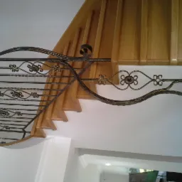 Kuta, ozdobna poręcz schodowa z motywem kwiatowym, zamontowana przy drewnianych schodach, widok od dołu.