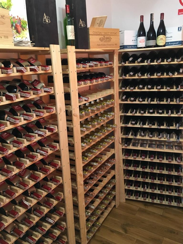 Półki wypełnione butelkami wina w piwniczce, widoczna drewniana skrzynka Chateau Haut Veyrac na górnej półce.