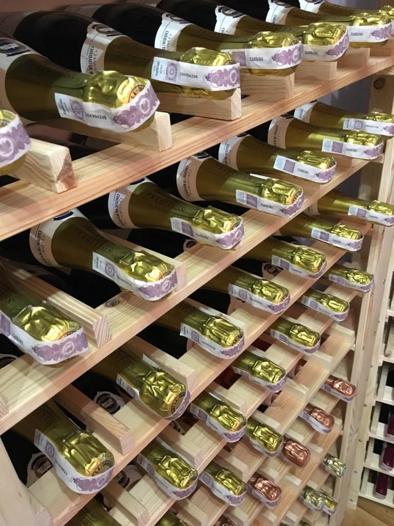 Rzędy butelek z szampanem leżące na drewnianych półkach regału; widoczne etykiety i złote kapsle.